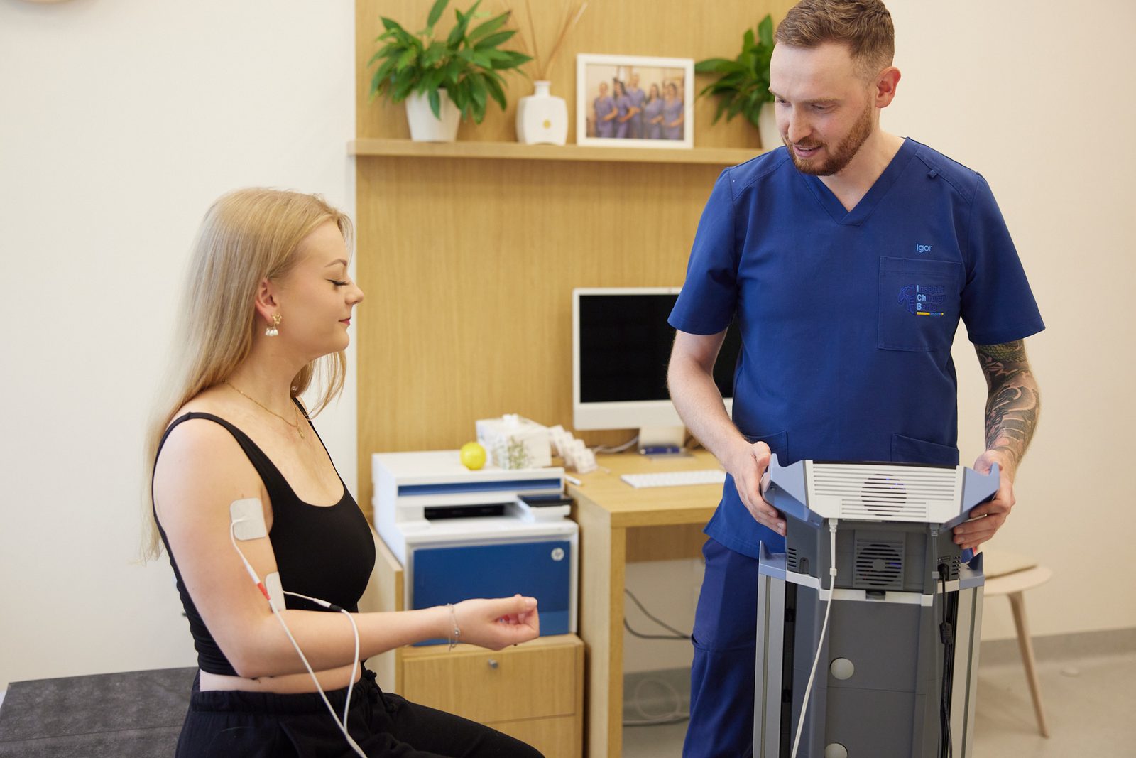 Fizjoterapeuta ustawia parametry elektroterapii, pacjentka z naklejonymi elektrodami